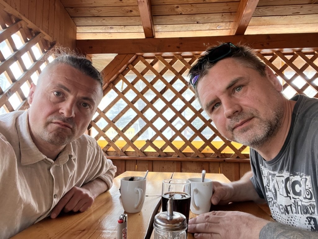 The two of us at a wooden table in a gazebo, two coffee mugs, a sugar jar, a lighter.